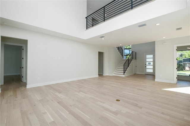 unfurnished living room featuring a high ceiling and light hardwood / wood-style flooring