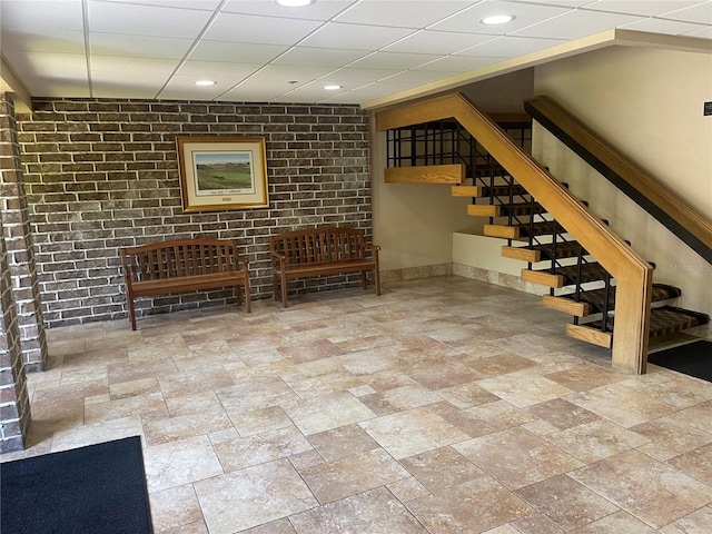 basement featuring brick wall, a paneled ceiling, and tile floors