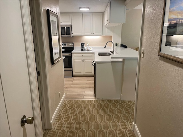 kitchen with kitchen peninsula, stainless steel appliances, white cabinetry, light wood-type flooring, and sink