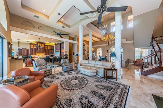 living room with a high ceiling, ceiling fan with notable chandelier, a raised ceiling, and light tile floors