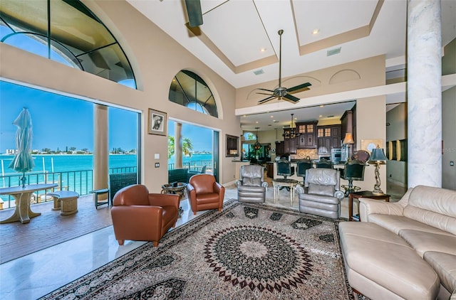 tiled living room with a water view, a high ceiling, ceiling fan, and a raised ceiling