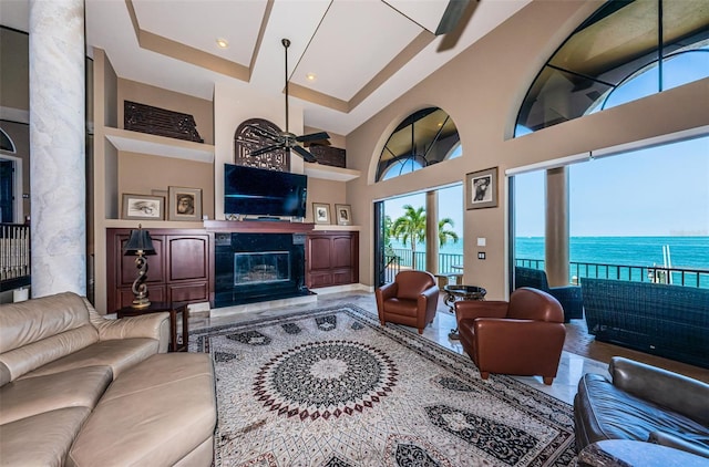 living room with a water view, a fireplace, ceiling fan, a raised ceiling, and a high ceiling