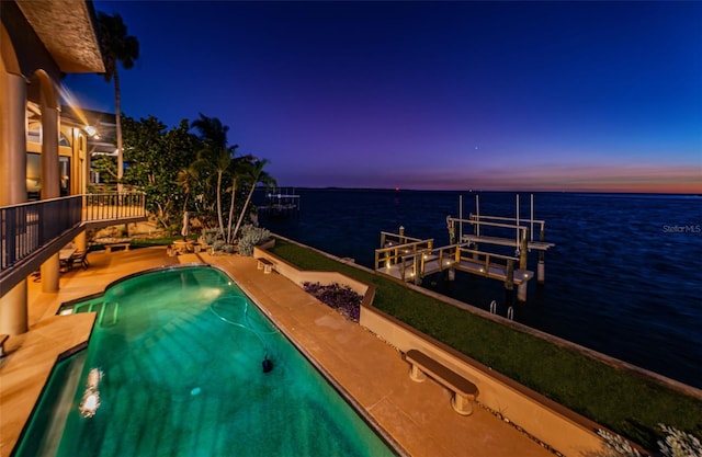 pool at dusk with a patio area, a water view, and a dock