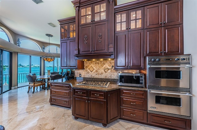 kitchen with a water view, light tile flooring, tasteful backsplash, dark stone countertops, and appliances with stainless steel finishes