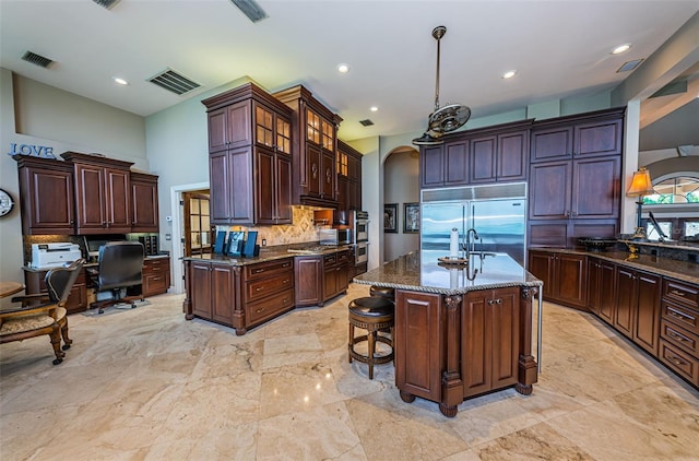 kitchen with stainless steel appliances, dark stone counters, an island with sink, and light tile floors