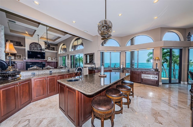 kitchen featuring dark stone countertops, a center island with sink, a water view, sink, and a kitchen bar