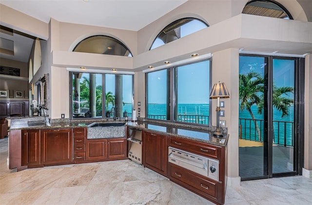 kitchen featuring kitchen peninsula, a water view, stone counters, light tile floors, and a high ceiling