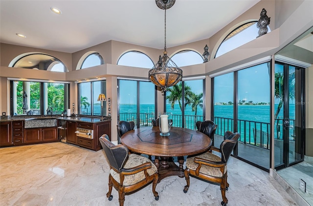 dining area featuring a towering ceiling, sink, light tile flooring, and a water view