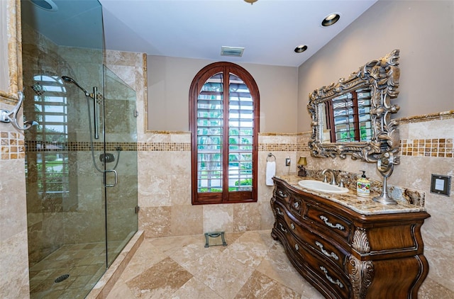 bathroom featuring a shower with shower door, vanity with extensive cabinet space, tile walls, and tile flooring