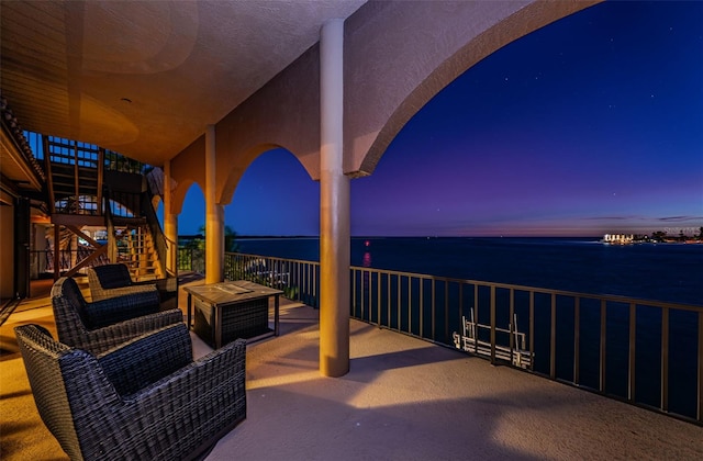 patio terrace at dusk featuring a water view and a balcony