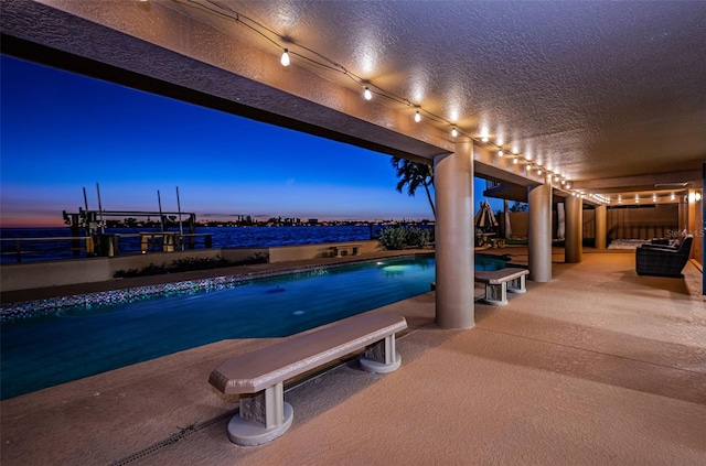 pool at dusk with a water view and a patio area