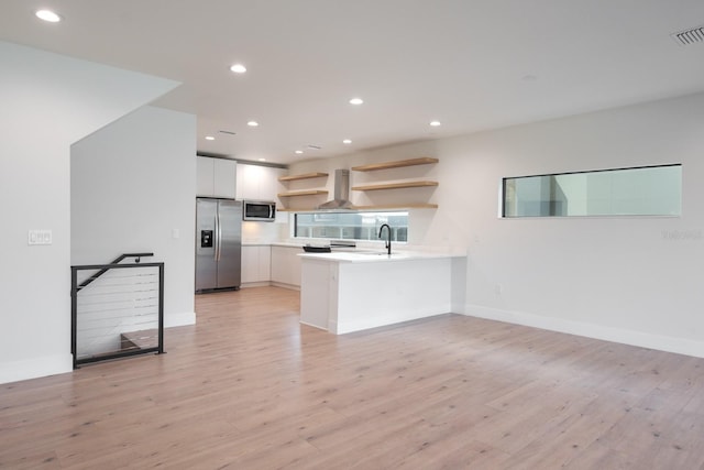 kitchen with light hardwood / wood-style floors, appliances with stainless steel finishes, kitchen peninsula, and wall chimney range hood