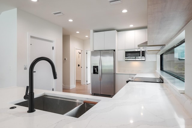 kitchen featuring appliances with stainless steel finishes, white cabinets, light stone countertops, and sink