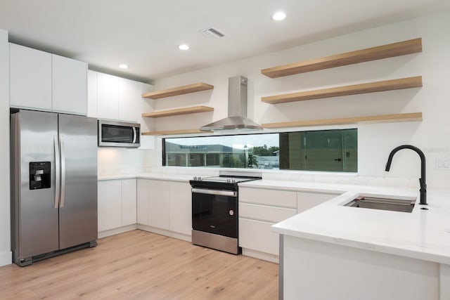 kitchen featuring white cabinetry, light wood-type flooring, wall chimney exhaust hood, sink, and appliances with stainless steel finishes