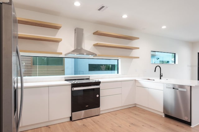 kitchen with white cabinetry, light wood-type flooring, wall chimney range hood, stainless steel appliances, and sink