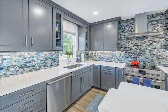 kitchen featuring stainless steel appliances, gray cabinets, backsplash, wall chimney range hood, and sink