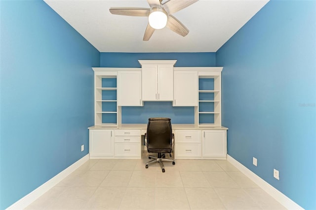 unfurnished office with built in desk, ceiling fan, and light tile floors