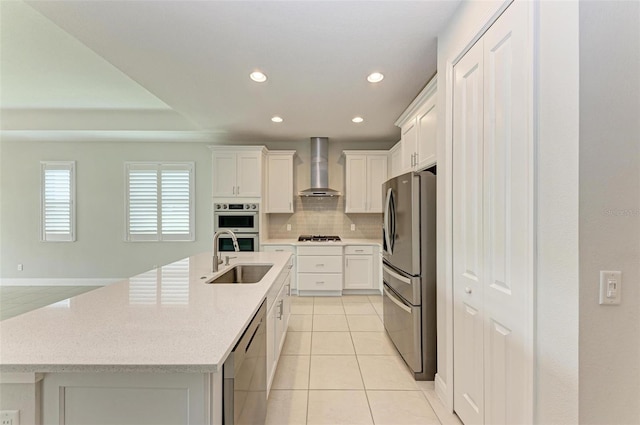 kitchen with tasteful backsplash, wall chimney exhaust hood, a kitchen island with sink, sink, and appliances with stainless steel finishes