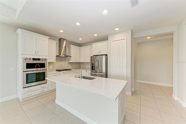 kitchen with wall chimney range hood, stainless steel appliances, tasteful backsplash, white cabinetry, and sink