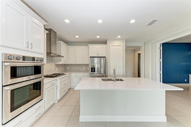 kitchen with wall chimney range hood, stainless steel appliances, a center island with sink, and sink