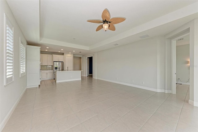 unfurnished living room featuring ceiling fan, a tray ceiling, and light tile flooring