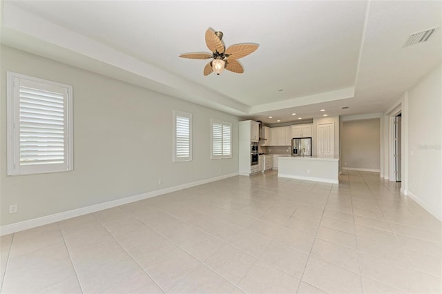 unfurnished living room featuring ceiling fan, light tile floors, and a raised ceiling