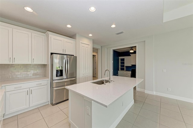 kitchen with light tile flooring, backsplash, an island with sink, stainless steel fridge, and sink