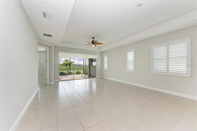 empty room featuring a tray ceiling, ceiling fan, and light tile floors