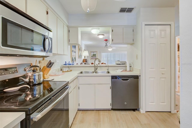 kitchen with appliances with stainless steel finishes, white cabinetry, sink, and light wood-type flooring