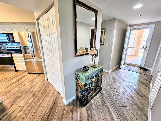 corridor featuring light hardwood / wood-style floors, a textured ceiling, and vaulted ceiling