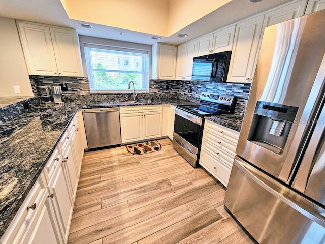 kitchen with light hardwood / wood-style floors, tasteful backsplash, dark stone countertops, white cabinetry, and appliances with stainless steel finishes