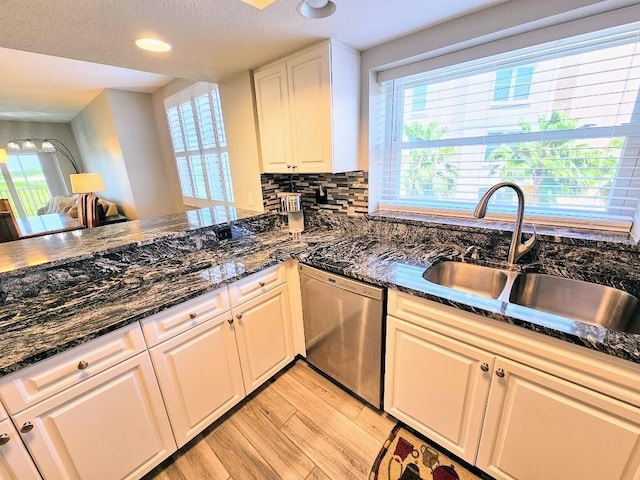 kitchen with light wood-type flooring, sink, dark stone countertops, and dishwasher