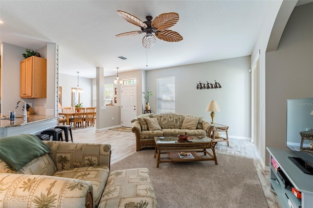 living room featuring ceiling fan with notable chandelier, a textured ceiling, and light hardwood / wood-style floors