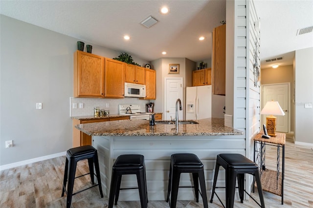 kitchen featuring a kitchen bar, white appliances, stone counters, light hardwood / wood-style flooring, and sink