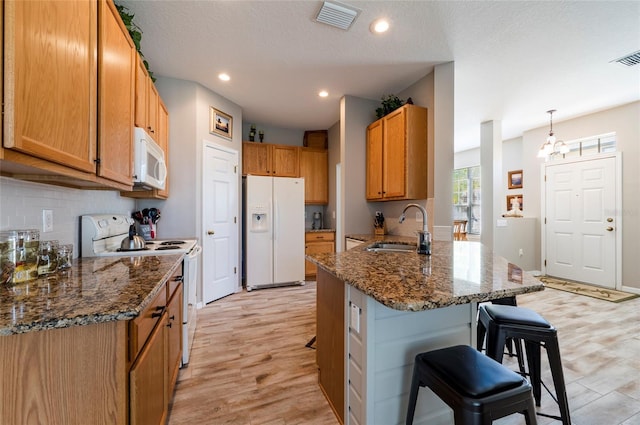 kitchen featuring a breakfast bar, kitchen peninsula, sink, white appliances, and light hardwood / wood-style flooring