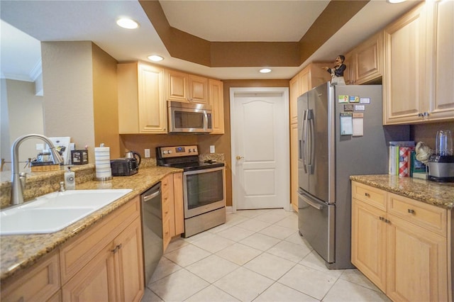 kitchen featuring light stone countertops, stainless steel appliances, sink, light brown cabinetry, and a raised ceiling