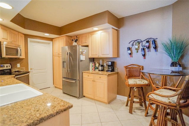 kitchen featuring stainless steel appliances, light stone counters, light tile flooring, and light brown cabinetry