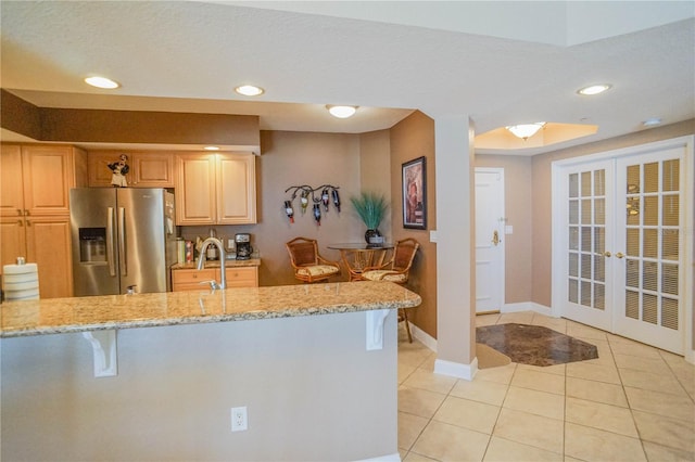 kitchen with light brown cabinets, french doors, light tile flooring, stainless steel refrigerator with ice dispenser, and light stone counters