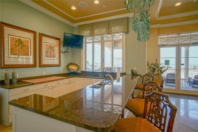 kitchen with tile flooring, dark stone countertops, ornamental molding, white cabinets, and sink