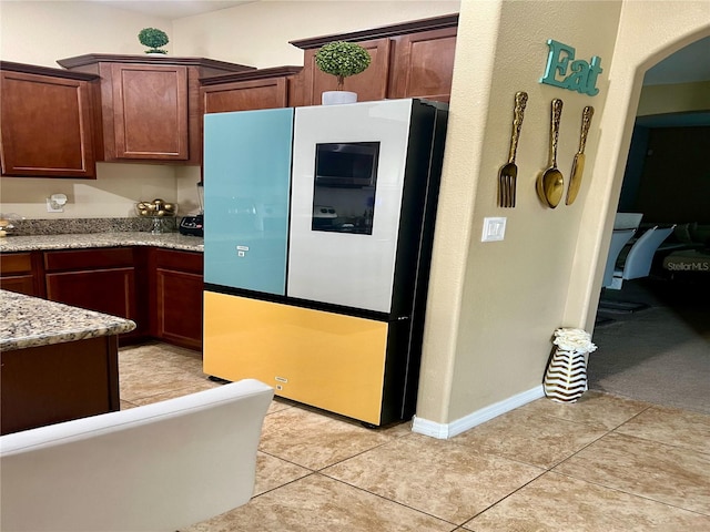 kitchen with light tile patterned flooring, light stone countertops, and fridge