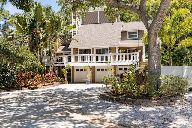 beach home with a garage, roof with shingles, driveway, and fence