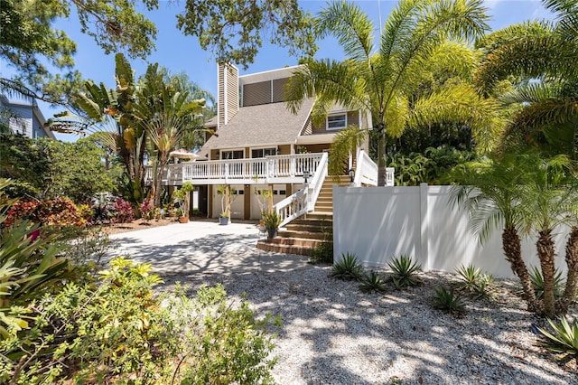 view of front of house with stairs, driveway, a chimney, and fence