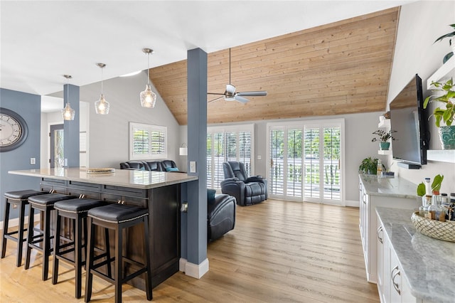 kitchen featuring open floor plan, hanging light fixtures, white cabinetry, and light stone countertops