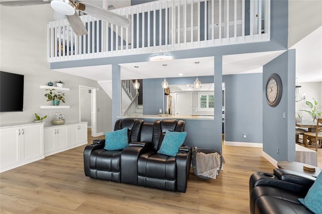 living area featuring a ceiling fan, baseboards, light wood finished floors, and stairs