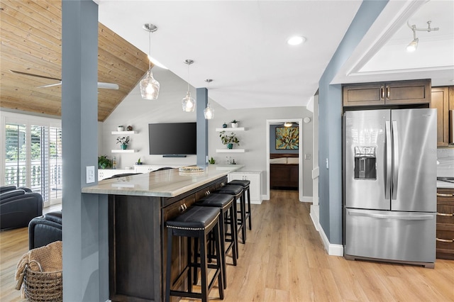 kitchen featuring light stone counters, stainless steel refrigerator with ice dispenser, hanging light fixtures, open floor plan, and a kitchen breakfast bar