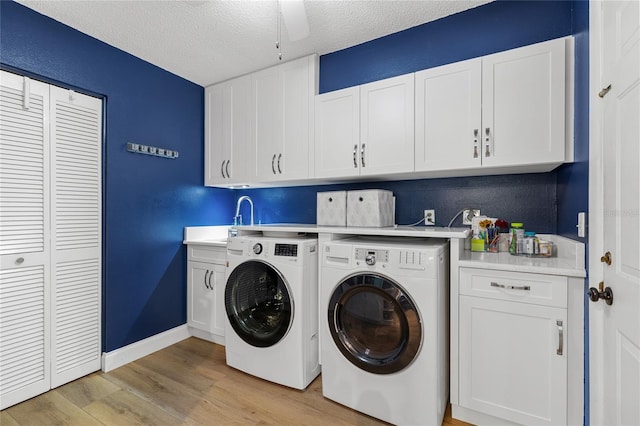 washroom featuring a textured ceiling, baseboards, cabinet space, light wood finished floors, and washing machine and clothes dryer