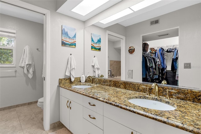 bathroom with a walk in closet, visible vents, a sink, and double vanity