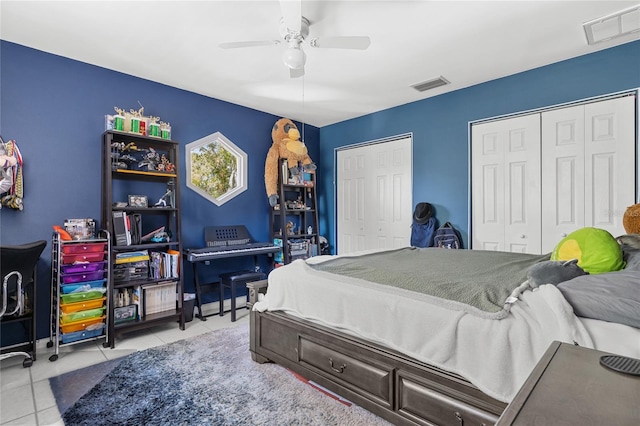 bedroom featuring light tile patterned floors, ceiling fan, visible vents, and two closets