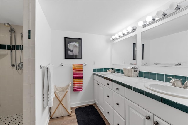 bathroom with double vanity, a tile shower, a sink, and wood finished floors