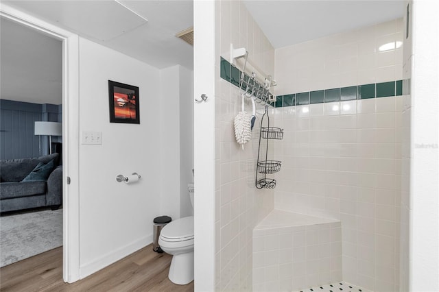 full bathroom with visible vents, toilet, a tile shower, wood finished floors, and baseboards